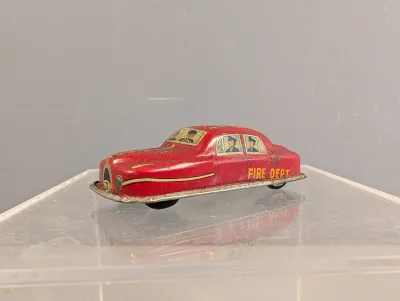 Sale Photo Thumbnail #368: Vintage lithographed tinplate fire department sedan toy, featuring illustrated figures inside the windows and moderate age-related wear.