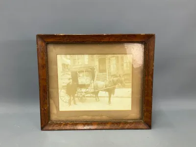 Sale Photo Thumbnail #356: Antique sepia-tone photograph depicting a horse-drawn delivery wagon and driver, housed in a stained oak wood frame with beaded inner trim.