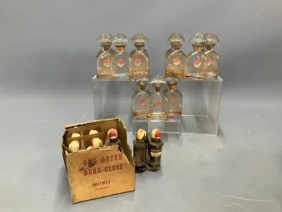 Sale Photo Thumbnail #158: Collection of vintage glass perfume bottles with fan-shaped stoppers alongside an original cardboard display box of Dura-Gloss Nutmeg nail polish bottles.