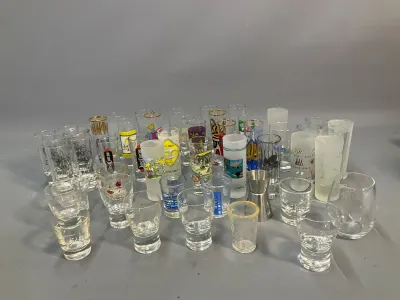 Sale Photo Thumbnail #69: Large collection of novelty shot glasses and barware featuring various souvenir graphics, liquor logos, and plain glass designs.
