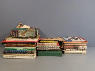 Sale Photo Thumbnail #298: Collection of vintage mid-century cookbooks and household hint books arranged in stacks, showing heavy shelf wear and aged bindings.