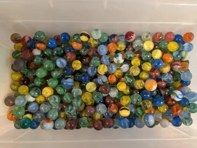 Sale Photo Thumbnail #308: Large collection of vintage glass marbles in assorted colors and patterns stored inside a clear plastic container.