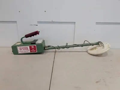 Sale Photo Thumbnail #484: Vintage Garrett Master Hunter TR metal detector featuring a green metal body, red grip handle, and white search coil.