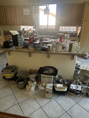 Sale Photo Thumbnail #59: Large collection of kitchenware, glassware, small appliances, and bakeware displayed on a granite-topped kitchen island and tile floor.