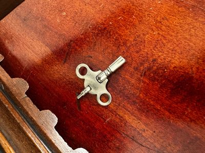 Sale Photo Thumbnail #77: Small metallic clock or music box winding key resting on a polished wooden surface.