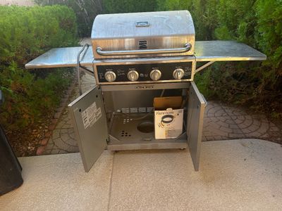 Sale Photo Thumbnail #3: Kenmore stainless steel four-burner gas grill with dual side shelves and open cabinet storage underneath.
