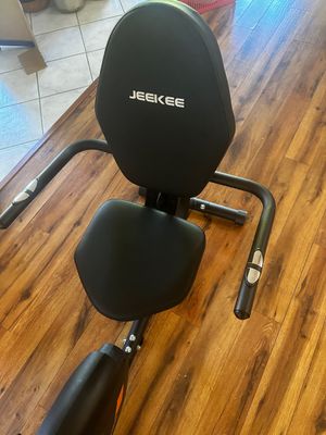 Sale Photo Thumbnail #21: JEEKEE recumbent exercise bike featuring a padded black seat, backrest, and side handlebars with pulse sensors.