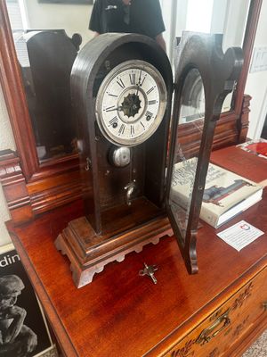 Sale Photo Thumbnail #78: Antique wooden mantel clock with a Roman numeral dial, visible pendulum, open glass door, and winding key included.