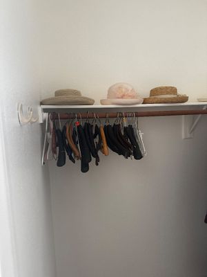 Sale Photo Thumbnail #65: Collection of women's vintage dress hats resting on a closet shelf above an assortment of wooden and plastic clothing hangers.