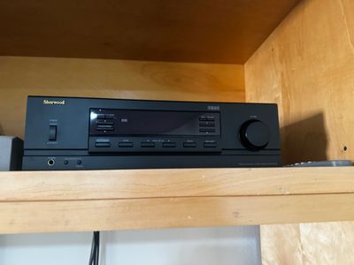 Sale Photo Thumbnail #45: Black Sherwood stereo receiver, model RX-4109, featuring digital display tuner and front panel control buttons, resting on a wooden shelf.