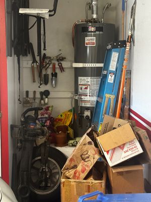 Sale Photo Thumbnail #61: Garage storage area featuring a Ruud water heater, a blue Werner step ladder, hand tools, potting supplies, and cardboard storage boxes.