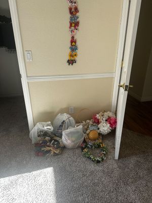 Sale Photo Thumbnail #69: Collection of decorative items, floral wreaths, and gift baskets resting on carpet, beneath a vertical felt animal wall hanging.