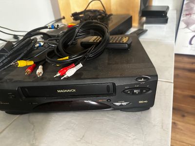 Sale Photo Thumbnail #43: Black Magnavox VHS HQ VCR deck with a remote control, RCA AV cables, and coaxial cords.