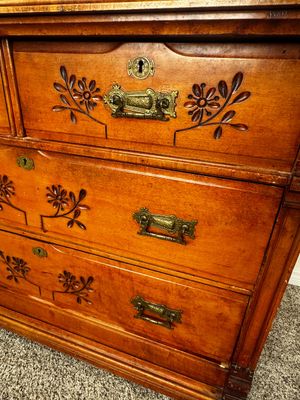 Sale Photo Thumbnail #30: Detail of an antique wooden dresser featuring carved floral motifs, ornate brass bail pulls, and keyhole escutcheons.