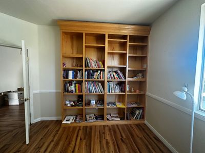 Sale Photo Thumbnail #47: Large wooden four-section built-in style bookcase with adjustable shelving, partially filled with books and decor.