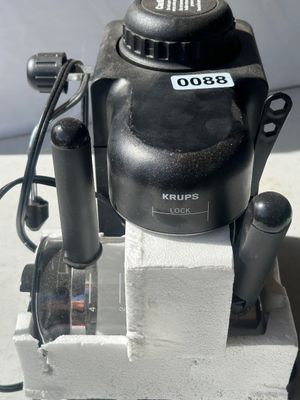 Sale Photo Thumbnail #115: Krups black countertop espresso/cappuccino maker, complete with glass carafe, filter holder, and steam wand. Features a steam cap safety lock. Item comes partially packed in original Styrofoam packaging. Lot tag 0088 attached.