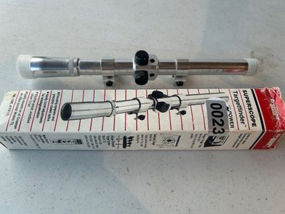 Sale Photo Thumbnail #23: Silver-tone metallic Crosman SUPERSCOPE Targetfinder 4X power air rifle scope, complete with its original factory box. Features mounting rings, protective lens caps, and anodized finish. Box shows minor shelf wear consistent with age.