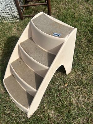 Sale Photo Thumbnail #127: A cream-colored molded plastic 4-step pet staircase featuring gray carpeted treads to provide traction for dogs or cats. Designed to assist pets in reaching beds, couches, or vehicles. Shows light wear and slight discoloration from normal use.