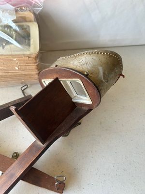 Sale Photo Thumbnail #156: An antique hand-held stereoscope viewer featuring an embossed metal hood with ornate floral and crest details stamped 'MONARCH', a wooden body, folding handle, glass lenses, and slide track. Accompanied by a stack of vintage stereoview/stereograph cards s
