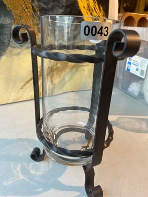 Sale Photo Thumbnail #43: A decorative glass cylinder vase or hurricane candle holder set inside a black wrought iron stand with scrolled legs and twisted metal rings. Appears to be in good pre-owned condition with no visible chips or cracks to the glass.