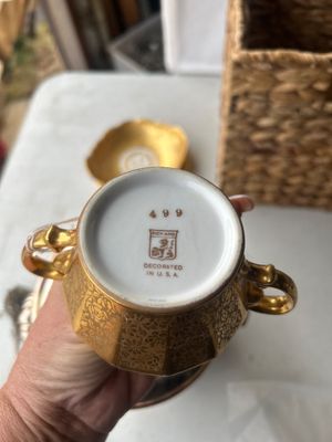 Sale Photo Thumbnail #166: A set of vintage gold-encrusted porcelain table service items including a two-handled sugar bowl stamped Pickard, Decorated in U.S.A. (number 499), a small bowl with a floral central motif labeled Wheeling Decorating Glass China, and a matching gold etche