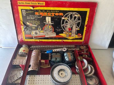 Sale Photo Thumbnail #94: A vintage A.C. Gilbert Erector Set No. 8 1/2 "All-Electric" construction toy set housed in its original red metal carrying case. The set includes various metal girders, plates, wheels, pulleys, and electric motor/engine units along with original lid graph