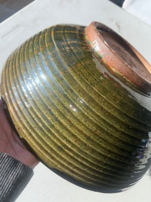 Sale Photo Thumbnail #61: Large wheel-thrown studio art pottery bowl featuring a ribbed exterior with dark olive green glaze and a warm tan-gold glazed interior. Signed 'Pask 83' (or similar artist signature) on the unglazed foot ring base. Dated 1983. Shows a small chip along the
