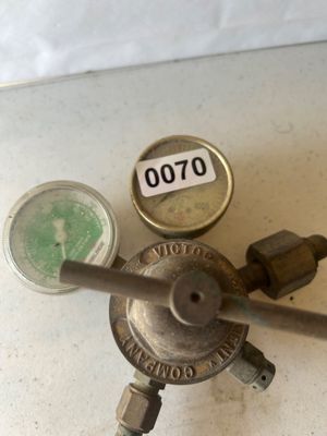 Sale Photo Thumbnail #86: A vintage Victor Equipment Company brass oxygen pressure regulator assembly, featuring dual pressure gauges and T-handle adjustment valve. Includes attached heavy-duty black rubber hosing and a handheld torch attachment with control valve. Shows age-appro