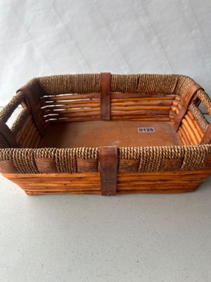 Sale Photo Thumbnail #187: A rectangular rustic woven basket tray featuring thick reed construction, dark leather or wood strapping, braided twine wrapping along the handles and rim, and a solid wood bottom panel. Shows minor surface wear consistent with age and use.