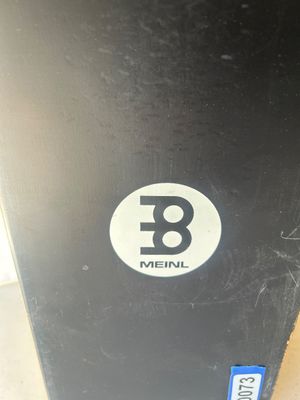 Sale Photo Thumbnail #90: A Meinl brand cajon percussion box instrument featuring a natural wood finish body with a black front playing surface and printed logo. Shows light edge wear from normal use.