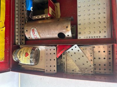 Sale Photo Thumbnail #92: A vintage A.C. Gilbert Erector Set No. 8 1/2 "All-Electric" construction toy set housed in its original red metal carrying case. The set includes various metal girders, plates, wheels, pulleys, and electric motor/engine units along with original lid graph