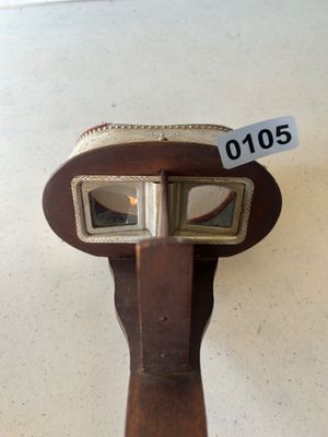 Sale Photo Thumbnail #154: An antique hand-held stereoscope viewer featuring an embossed metal hood with ornate floral and crest details stamped 'MONARCH', a wooden body, folding handle, glass lenses, and slide track. Accompanied by a stack of vintage stereoview/stereograph cards s