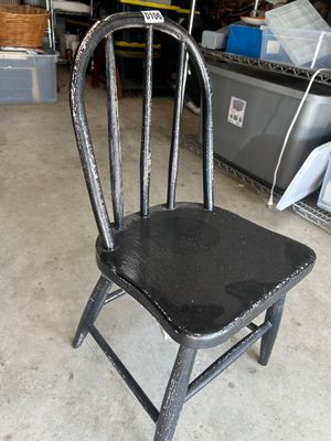 Sale Photo Thumbnail #162: A vintage black painted wooden chair with a spindle back design, likely sized for a child or doll display. The chair shows distress and wear to the black paint, revealing the light wood underneath, adding vintage character. Solid wood construction.