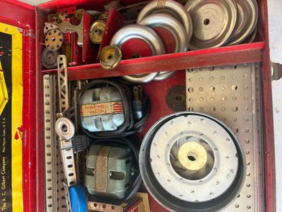 Sale Photo Thumbnail #96: A vintage A.C. Gilbert Erector Set No. 8 1/2 "All-Electric" construction toy set housed in its original red metal carrying case. The set includes various metal girders, plates, wheels, pulleys, and electric motor/engine units along with original lid graph