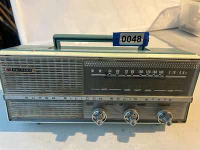 Sale Photo Thumbnail #48: A vintage mid-century Raleigh Super Silicon Solid State 7-transistor portable AM radio featuring a teal blue and cream plastic casing with a fold-down carrying handle, front speaker grille, dial tuning, and control knobs. Shows light cosmetic surface wear