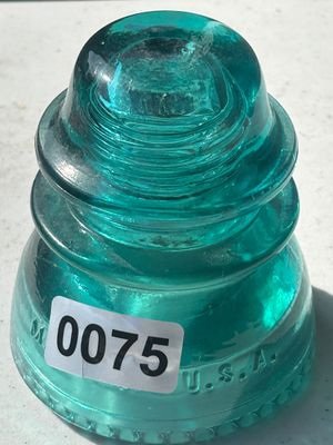Sale Photo Thumbnail #97: A vintage aqua blue/green glass glass insulator, embossed with 'MADE IN U.S.A.' along the base. Features a threaded interior and ribbed bottom rim. Shows light age-appropriate wear with a clean appearance.