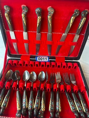 Sale Photo Thumbnail #11: A unique vintage flatware set featuring hand-carved horn handles shaped like stylized birds/roosters with brass and colorful inlaid accents. The set includes knives, spoons, and forks presented in a red velvet-lined fitted display box.