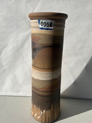 Sale Photo Thumbnail #56: A tall, hand-thrown studio pottery cylindrical vase featuring layered earth-tone bandings in shades of brown, beige, and tan with textured matte surfaces and drip-glaze detailing near the base. Appears to be in good condition with no visible cracks or chi