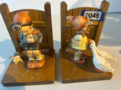 Sale Photo Thumbnail #45: A pair of vintage Goebel Hummel wooden bookends featuring iconic ceramic figures attached to wooden gate bases. One side depicts a young boy in lederhosen with a small pig, and the other shows a young girl with two geese (Goose Girl design). Both are set 