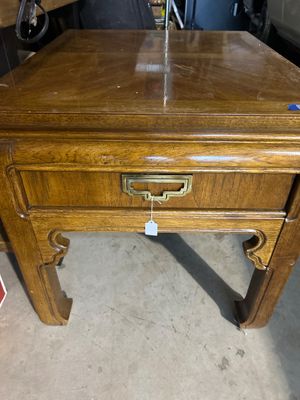 Sale Photo Thumbnail #193: A vintage Thomasville oak end table featuring Asian-inspired design elements, including chow-leg styled base details and a campaign-style brass drawer pull. The table includes a single drawer stamped with the Thomasville logo inside, and a parquetry/patte