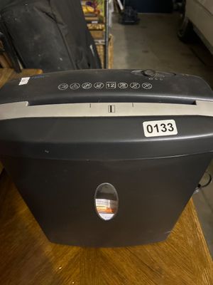 Sale Photo Thumbnail #197: A black Unitech cross-cut paper shredder featuring a 12-sheet capacity slot, safety warning icons, power/reverse switch, and a front viewing window for waste bin monitoring. Shows minor cosmetic wear from prior use.