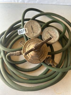Sale Photo Thumbnail #88: A Victor Equipment Company brass dual-gauge gas pressure regulator with attached coiled green rubber hose. Features two analog pressure gauges reading PSI/kPa. Shows signs of previous industrial/shop use and patina on brass components.