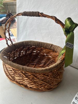 Sale Photo Thumbnail #184: Oval woven wicker basket featuring an integrated overhead carrying handle wrapped with cord, cord-trimmed rim, and decorative green satin ribbon.
