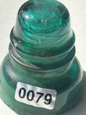 Sale Photo Thumbnail #101: A vintage heavy green glass insulator, commonly used on telegraph and telephone lines. Features a rich blue-green/teal color with internal bubbles and embossed detailing around the dome. Appears to be in good vintage condition with minor surface wear typi