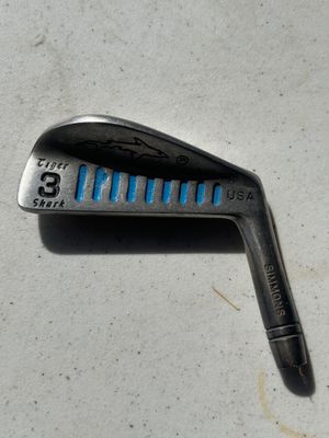Sale Photo Thumbnail #113: A collection of vintage golf iron club heads including Simmons Tiger Shark USA models (3-iron, 8-iron, 9-iron, and others). Metal construction with signature blue cavity slot fill and etched shark logo details. Heads show play wear and surface patina typi
