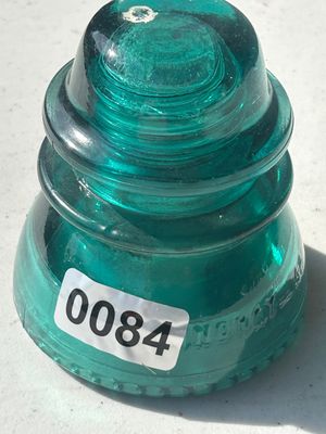 Sale Photo Thumbnail #106: A vintage aqua / green glass insulator, featuring ribbed glass detailing and embossed lettering around the base. Shows typical minor surface wear consistent with age and use.