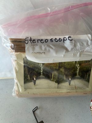 Sale Photo Thumbnail #155: An antique hand-held stereoscope viewer featuring an embossed metal hood with ornate floral and crest details stamped 'MONARCH', a wooden body, folding handle, glass lenses, and slide track. Accompanied by a stack of vintage stereoview/stereograph cards s