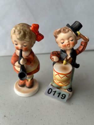 Sale Photo Thumbnail #180: A charming pair of vintage hand-painted ceramic or porcelain figurines featuring young musicians. One figurine depicts a young girl in an orange dress and red hair bow playing a horn or clarinet, and the other depicts a young boy tipping his top hat while