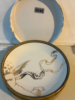 Sale Photo Thumbnail #46: A white fine porcelain decorative coaster or mini plate featuring a gold-gilt winged cherub design with a flowing ribbon. Comes in its original round presentation box with protective corrugated lining. Excellent condition with minor wear to the box.