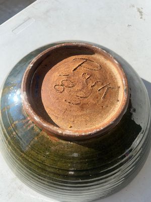 Sale Photo Thumbnail #60: Large wheel-thrown studio art pottery bowl featuring a ribbed exterior with dark olive green glaze and a warm tan-gold glazed interior. Signed 'Pask 83' (or similar artist signature) on the unglazed foot ring base. Dated 1983. Shows a small chip along the